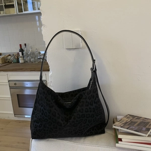 Macro shot of large leopard print tote bag featuring matte suede texture and metal buckle