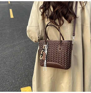 Close-up of brown quilted tote bag with textured V-shape stitching and designer charms