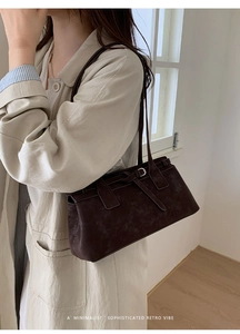 Detail der dunkelbraunen Wildleder-Schultertasche mit Schnalle an einem Modell