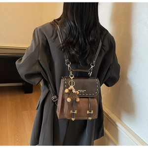 Dettaglio di uno zaino vintage in pelle marrone con cuciture bianche e ciondolo peluche
