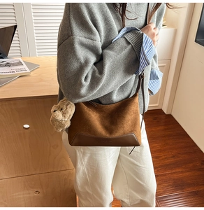 Detail view of brown suede shoulder bag with plush bear charm and leather stitching
