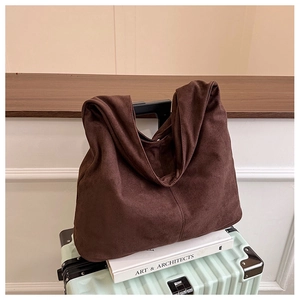 Detail of a dark brown suede tote bag with fine stitching on a mint green suitcase
