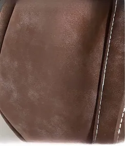 Close-up of brown suede fabric showing detailed white contrast stitching on the bag