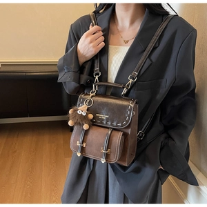 Dettaglio dello zaino marrone vintage con cuciture a vista e ciondolo a mostriciattolo