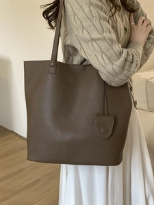 Elegant brown leather tote bag with bucket shape and small pouch charm on model