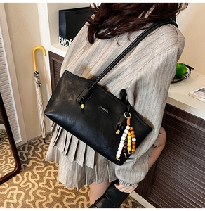 Close-up of a black faux-leather tote bag featuring a beaded tassel and brand logo