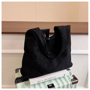 Detail of a large black suede hobo shoulder bag placed on an art book in a minimalist setting