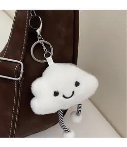 Close-up of white plush cloud charm with smiley face and striped legs on brown suede bag