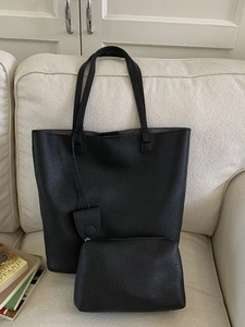 Black pebble leather tote bag set with matching pouch on a white fabric sofa