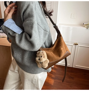 Detail view of brown suede shoulder bag with leather base and cute plush dog charm