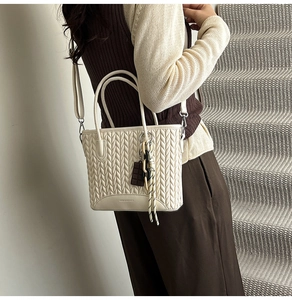 Detail of beige quilted bucket bag showing V-pattern texture and chocolate charm