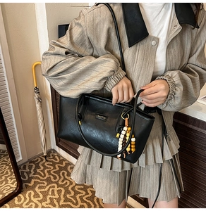Detail of black PU leather tote bag with colorful beaded charm and metal logo plaque