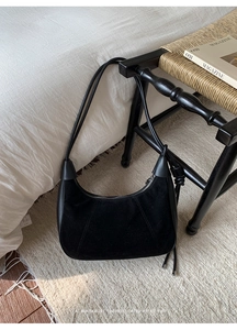 Detailed view of black suede hobo bag with smooth leather trim on a wooden chair