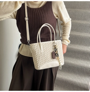 Detail of off-white quilted bucket bag with chocolate charm and adjustable strap
