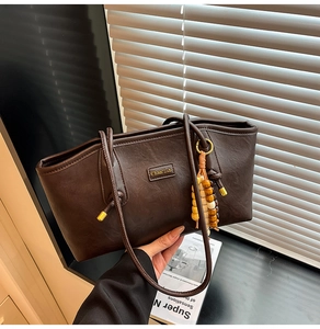 Close-up of brown PU leather tote bag with gold metal logo and beaded tassel detail