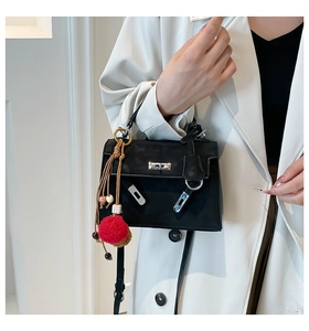 Detail of matte black Kelly style handbag with red pompom charm on a white blazer outfit