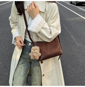 Detail of dark brown suede shoulder bag with plush puppy pendant on urban street background