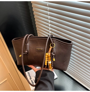Detail of dark brown leather tote featuring bead tassel and vintage metal branding logo