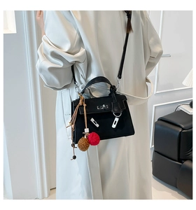 Detail of a black trapezoid leather handbag featuring a silver twist lock and furry charm