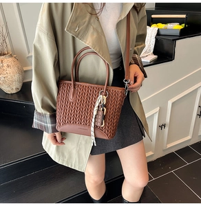 Detail of a brown woven texture bucket bag with a silk scarf accessory and brand lettering