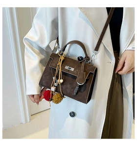Close-up of dark brown suede bag with silver turn-lock and colorful pompom charms