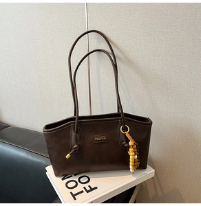 Detail of dark brown leather tote bag with colorful wooden bead tassel and metal logo