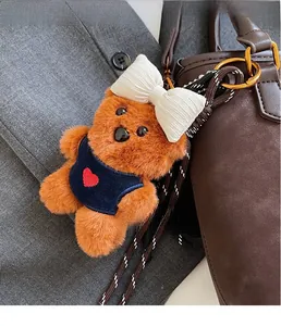 Detail of plush bear charm with a blue vest and bow on a brown textured leather bag