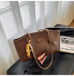 Detail of vintage brown tote bag with beaded charm and leather texture on desk