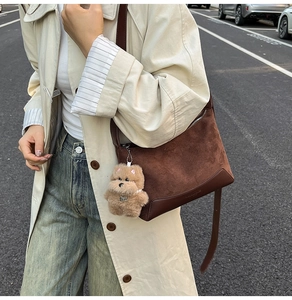 Close-up of brown suede shoulder bag with smooth leather trim and plush dog charm