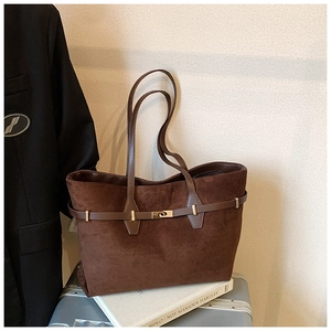 Close-up of brown suede tote bag with metal buckle detail and leather handle on books