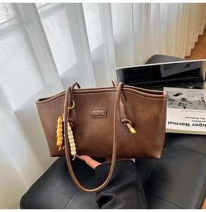 Macro detail of brown leather tote bag with gold metal plate and wooden bead pendant