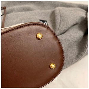 Detail view of the brown leather bag base with protective gold metal rivets and plush trim