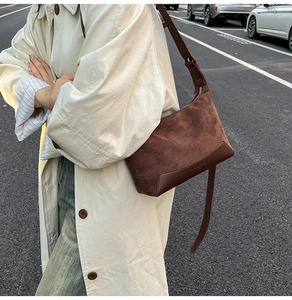 Detail view of brown suede underarm bag with smooth leather trim on a beige trench coat