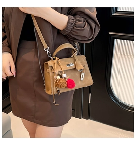 Brown textured Kelly handbag with top handle and plush charm worn by a model