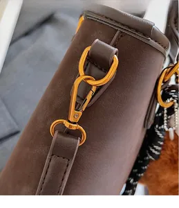 Detail of dark brown suede handbag featuring gold metal hook and woven strap accents