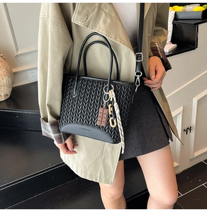 Detail of a black woven leather bucket bag with silver buckles and a stylish charm