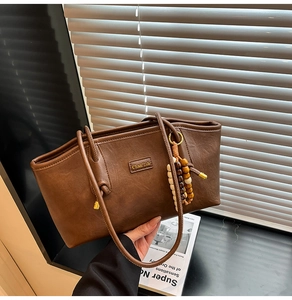 Close-up of brown vintage leather tote with wooden bead pendant and brand logo detail