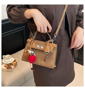 Detail of a brown leather trapezoid handbag featuring a metal twist lock and plush charm