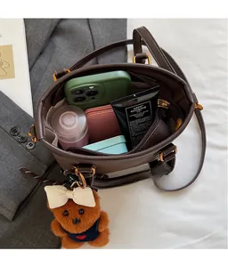 Interior view of brown bucket bag showing capacity with phone, wallet, and teddy charm