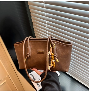 Detail of a brown leather tote bag featuring a unique colorful beaded charm accessory