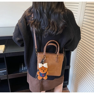 Close-up of brown faux leather tote bag with a cute bear charm on a female model