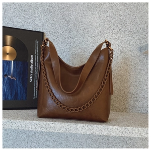 Detailed view of dark brown faux leather hobo bag with thick decorative chain and logo