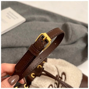 Close-up of golden metal buckle on dark brown leather strap of a plush bucket bag