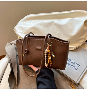 Macro detail of brown leather tote bag with wooden bead charm and metallic logo plate