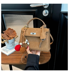Detail of khaki suede Kelly style handbag with plush pompom bag charm and metal lock