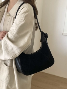 Chic black faux suede crescent shoulder bag worn with a classic trench coat