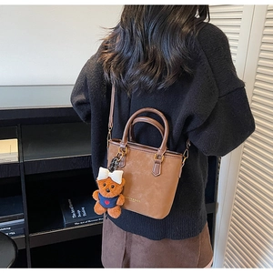 Detail view of a vintage brown leather bucket bag with cute bear charm and shoulder strap