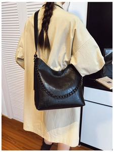 Large black bucket bag with chunky chain detail shown on model in minimalist home setting
