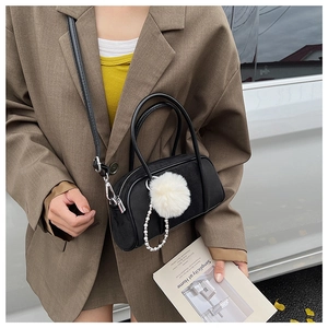 Detail of black suede bowling bag with white pompom and pearl chain accessories