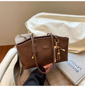 Close-up of brown retro faux leather tote bag with gold logo and beaded tassel charm